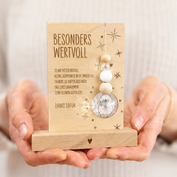 Beispielfoto mit Händen - Holzkarte mit der Gravur „Besonders wertvoll“, funkelndem Kristall und filigranen Sternmotiven, optional mit passendem Kartenhalter aus Holz – besonderes Dankeschön-Geschenk für Erzieherinnen, Lehrerinnen und liebe Menschen.