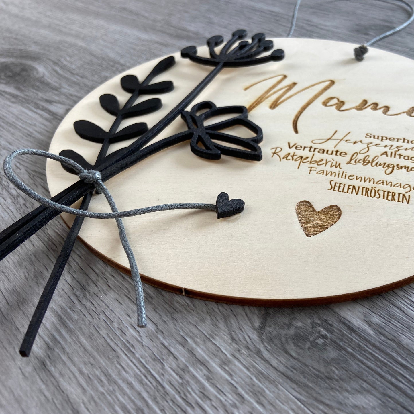 Holzschild Mama mit Synonymen passend zu "Mama"  u.a. Herzensmensch, Superheldin, Familienmanagerin - Geschenkidee zum Muttertag mit individueller Gravur Wunschtext, Detailansicht schwarze Holzblumen Verzierung auf dem Schild
