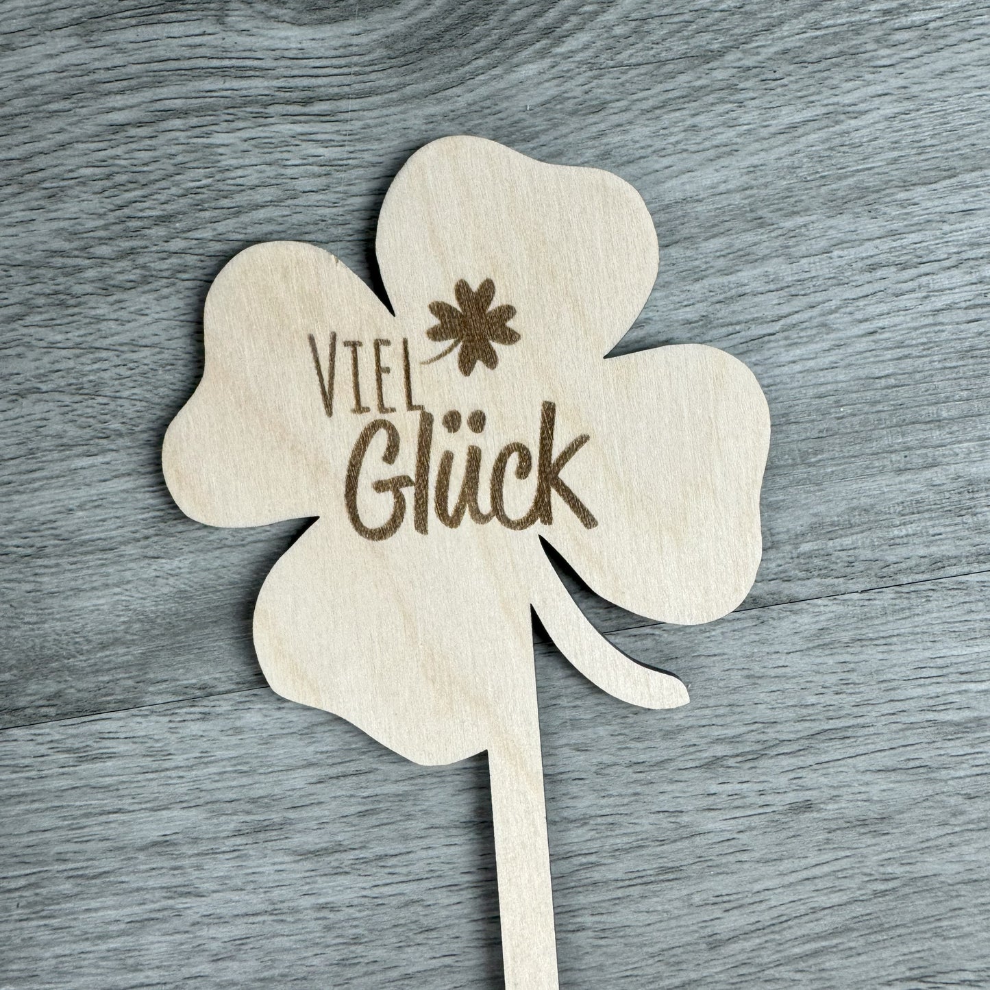Detailansicht eines Holz-Blumensteckers in Kleeblattform mit der Gravur "Viel Glück" – ein Geschenk, das Glück wünscht.