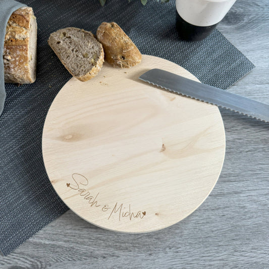 Personalisierbares rundes Holzbrett mit gravierter Namensschrift und Herzmotiv – Geschenkidee für Paare.
