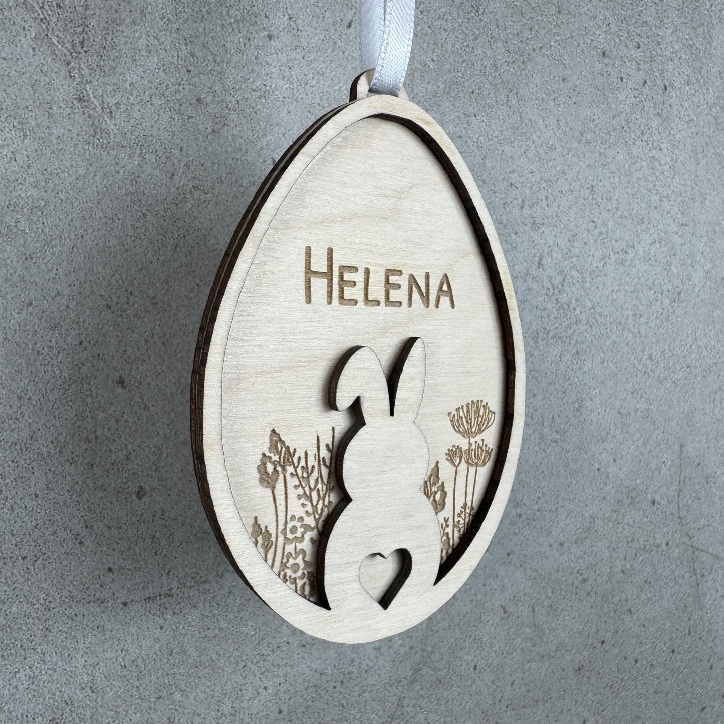 hängend, leichte Seitenansicht - Osteranhänger Hase auf Blumenwiese, mit Name personalisiert oder mit dem Text Frohe Ostern Gravur aus Holz, Lasergravur