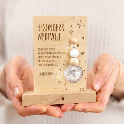 Beispielfoto mit Händen - Holzkarte mit der Gravur „Besonders wertvoll“, funkelndem Kristall und filigranen Sternmotiven, optional mit passendem Kartenhalter aus Holz – besonderes Dankeschön-Geschenk für Erzieherinnen, Lehrerinnen und liebe Menschen.