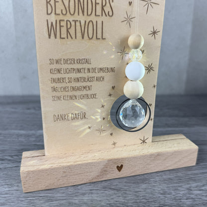 Detailansicht - Holzkarte mit der Gravur „Besonders wertvoll“, funkelndem Kristall und filigranen Sternmotiven, optional mit passendem Kartenhalter aus Holz – besonderes Dankeschön-Geschenk für Erzieherinnen, Lehrerinnen und liebe Menschen.