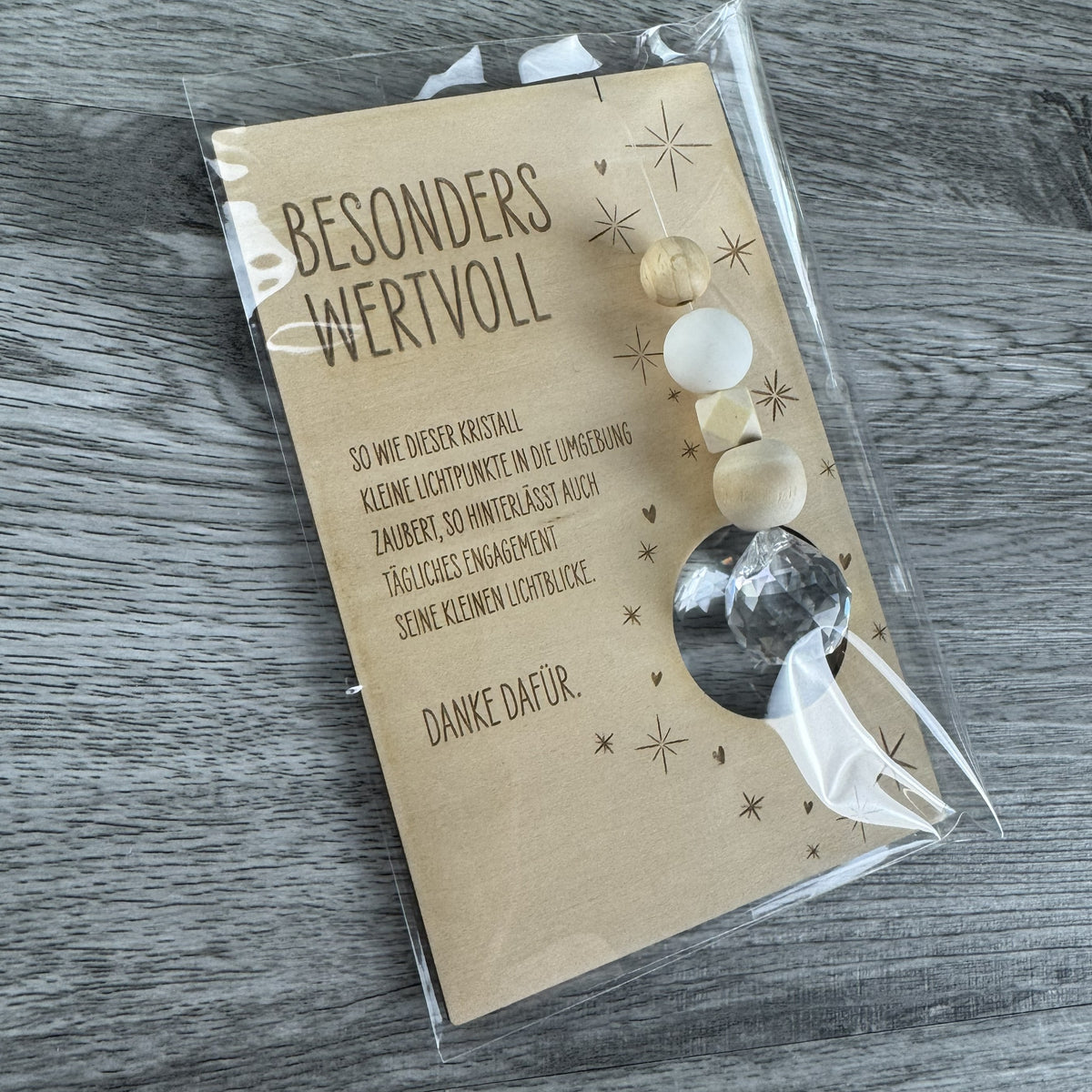 Produktfoto Karte verpackt ohne Halter - Holzkarte mit der Gravur „Besonders wertvoll“, funkelndem Kristall und filigranen Sternmotiven, optional mit passendem Kartenhalter aus Holz – besonderes Dankeschön-Geschenk für Erzieherinnen, Lehrerinnen und liebe Menschen.