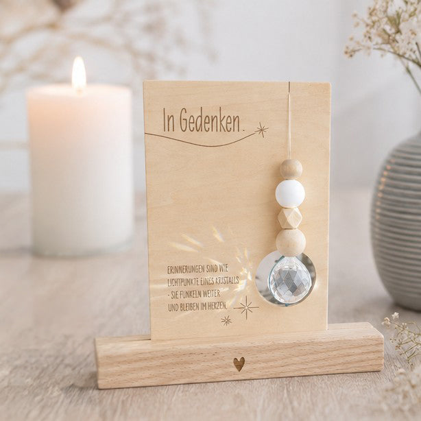 Holzkarte „In Gedenken“ mit einem funkelnden Kristall und dem Spruch über Erinnerungen, die wie Lichtpunkte weiterfunkeln und im Herzen bleiben, optional mit Kartenhalter aus Holz als Erinnerungsgeschenk für Trauernde.