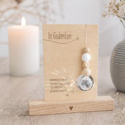 Holzkarte „In Gedenken“ mit einem funkelnden Kristall und dem Spruch über Erinnerungen, die wie Lichtpunkte weiterfunkeln und im Herzen bleiben, optional mit Kartenhalter aus Holz als Erinnerungsgeschenk für Trauernde.