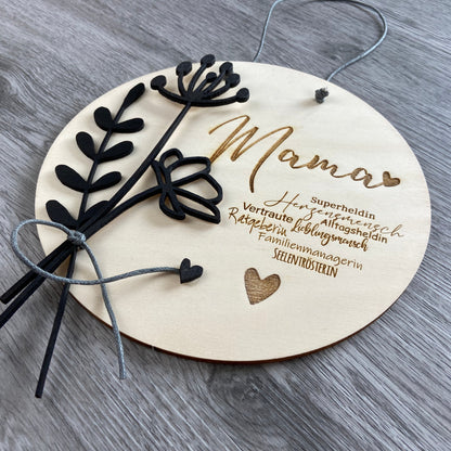 Holzschild Mama mit Synonymen passend zu "Mama"  u.a. Herzensmensch, Superheldin, Familienmanagerin - Geschenkidee zum Muttertag mit individueller Gravur Wunschtext, mit schwarzen Blumen verziert, Schrägansicht